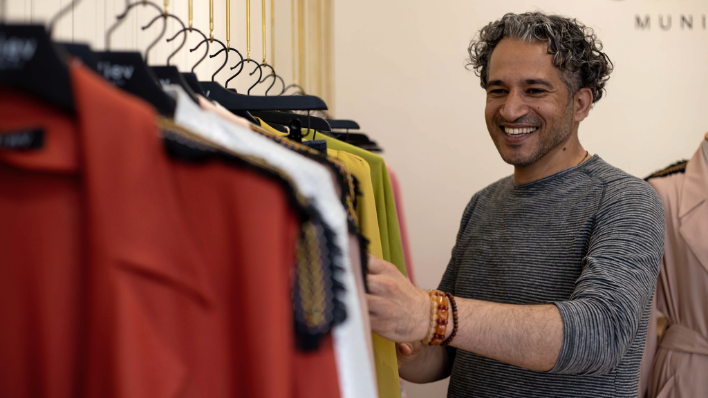 Mohamad Alhamod lacht und sortiert seine bunten selbst geschneiderten Kleidungsstücke